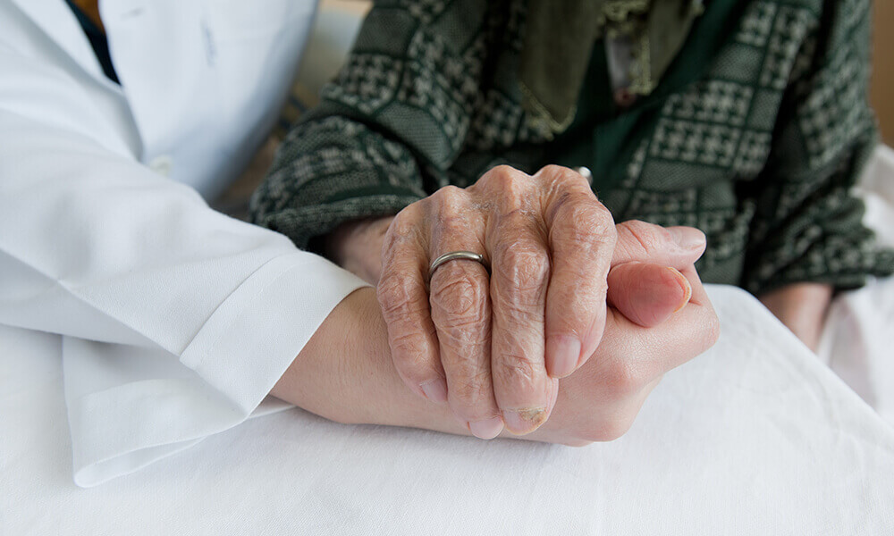 elderly person's hand holding doctor's hand