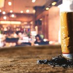 cigarette bud burning into a tabletop in a bar